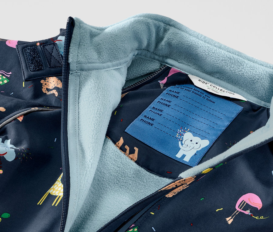 Detailansicht eines Kinder-Softshell-Einteilers mit Tiermotiven, Reißverschluss und Namensschild sichtbar.