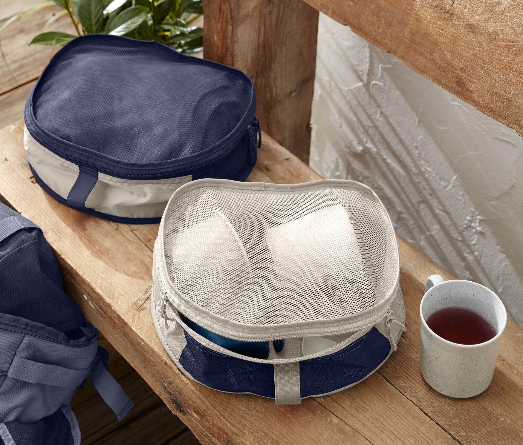Zwei Rucksack-Organizer liegen auf einer Holzbank neben einer Tasse und einem Rucksack.