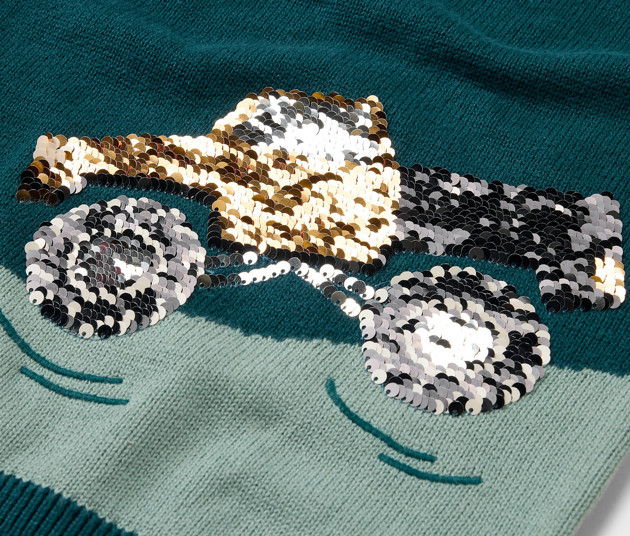 Detailansicht eines Kinder-Strickpullovers mit einem glitzernden Lastwagen-Motiv.
