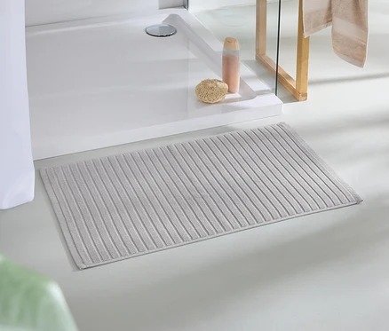 Eine beige Badematte liegt auf dem Boden neben einer Dusche.