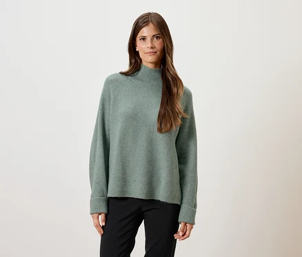 Frau trägt einen grünen Pullover und eine schwarze Hose.