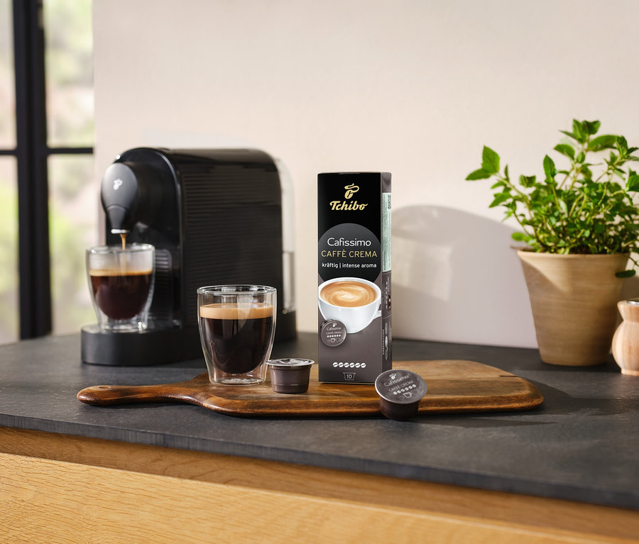 Kaffeemaschine bereitet Kaffee in ein Glas neben einer Packung Cafissimo Caffè Crema kräftig - 10 Kapseln zu.