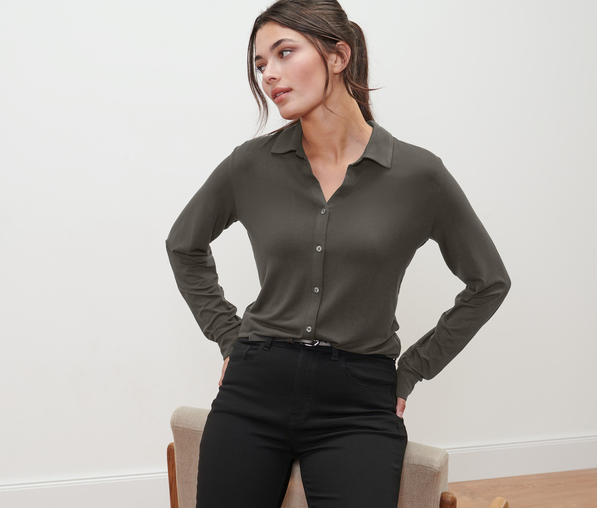 Frau posiert in olivgrünem Blusenshirt mit Knopfleiste und schwarzen Hosen.