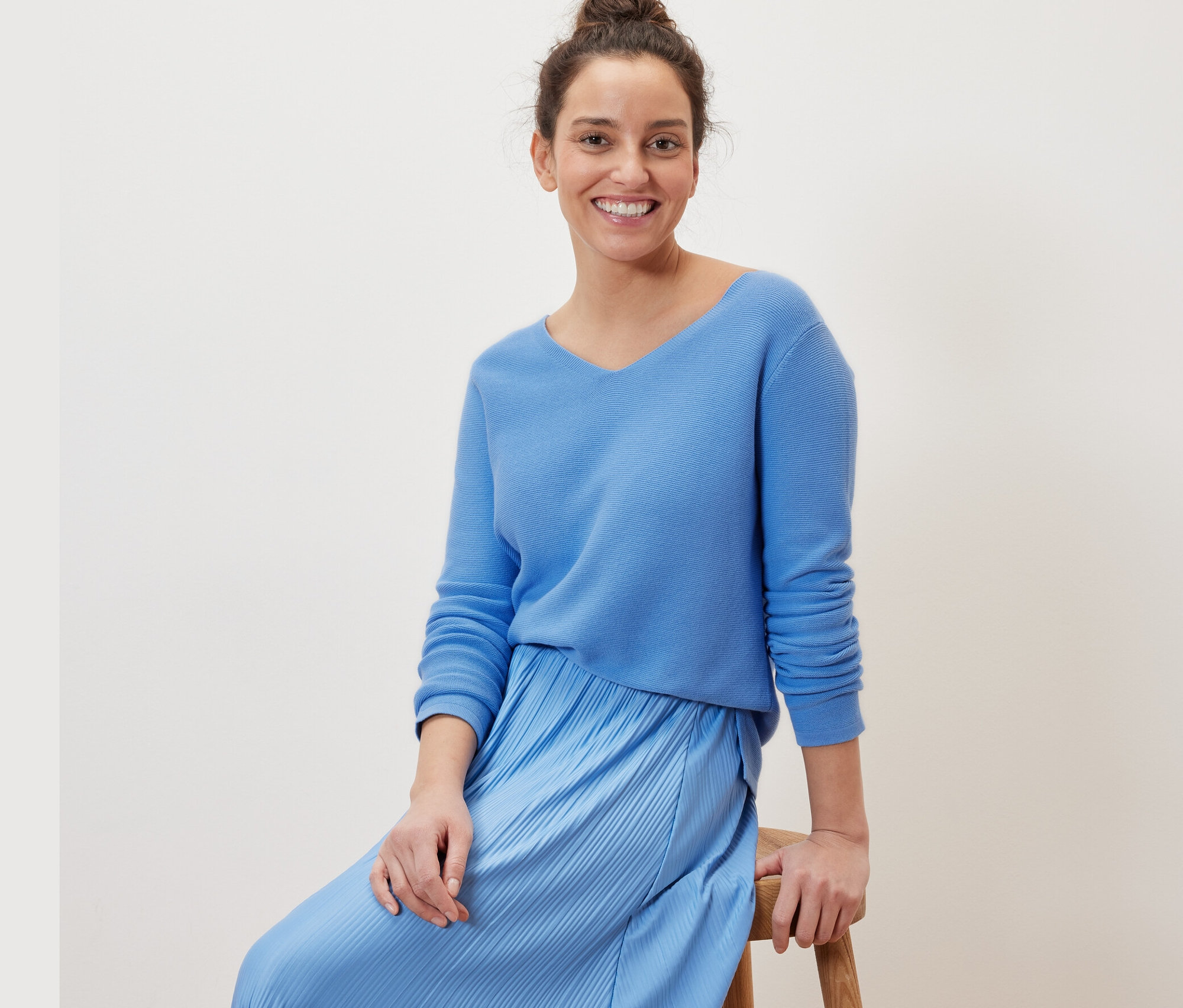 Frau sitzt auf einem Hocker und trägt einen hellblauen Strickpullover.