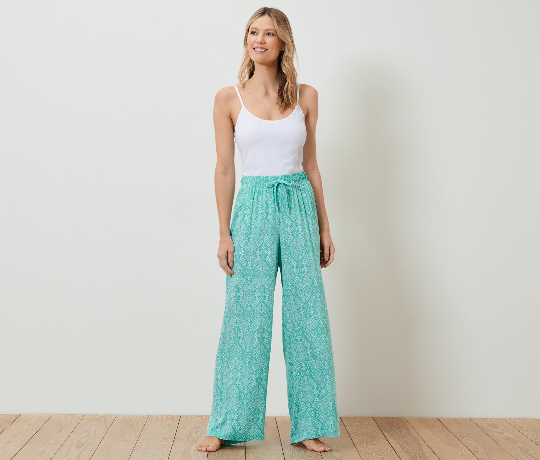 Frau steht und trägt ein weißes Top und eine Relaxhose.