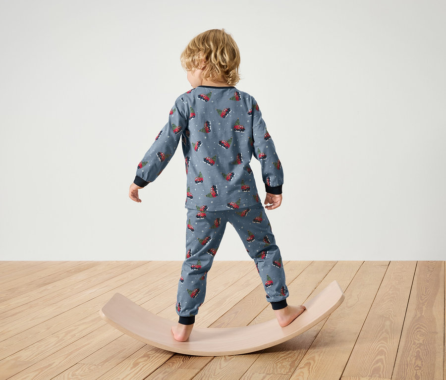 Junge im Weihnachtspyjama steht auf einem hölzernen Balance Board.