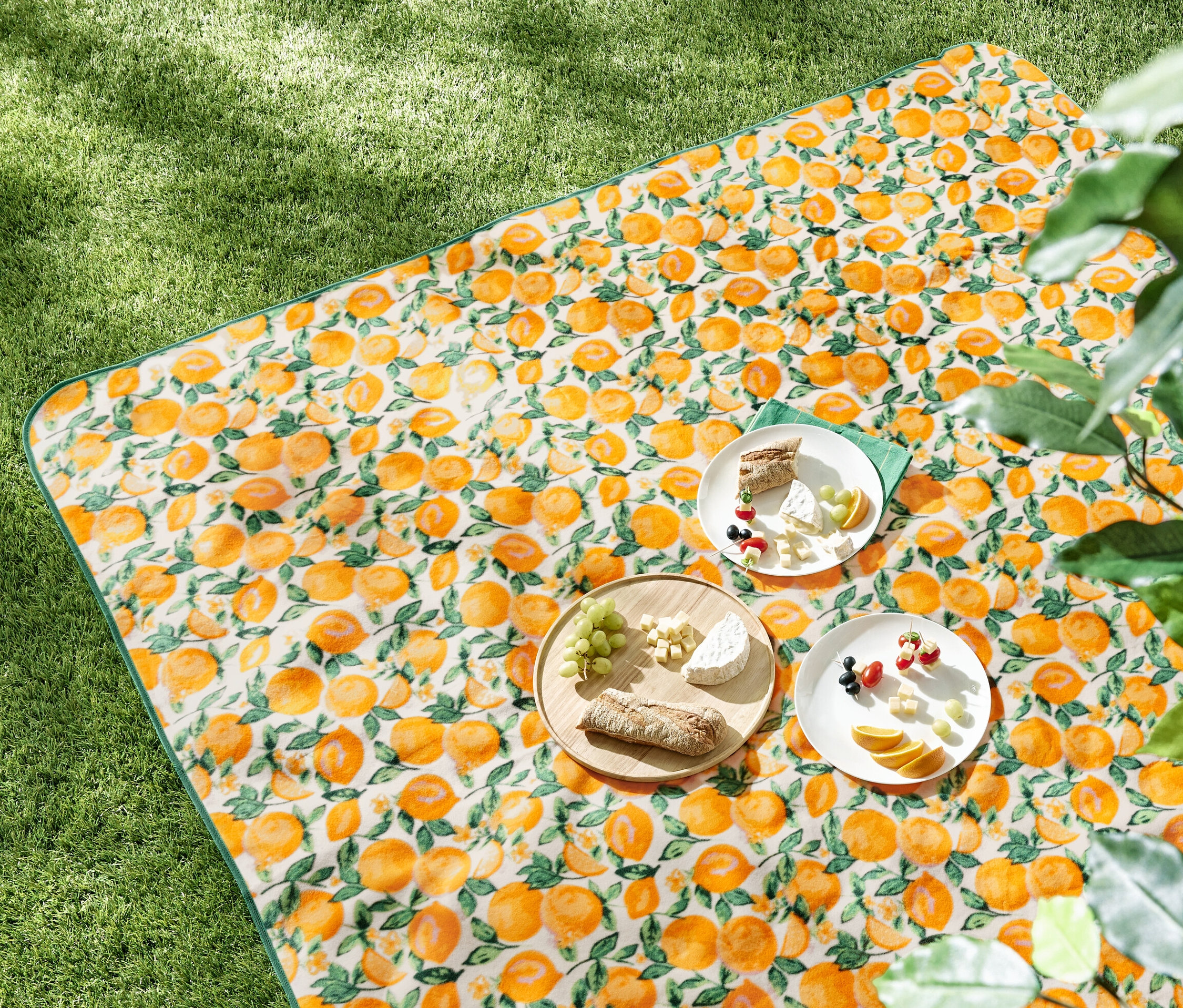 XL-Picknickdecke mit Orangenmuster und Speisen darauf im Gras.