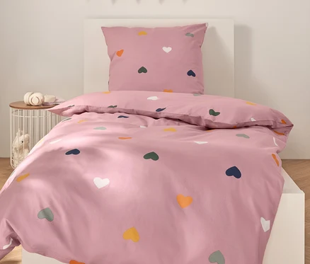 Rosa Bettwäsche mit bunten Herzen auf einem weißen Bett.