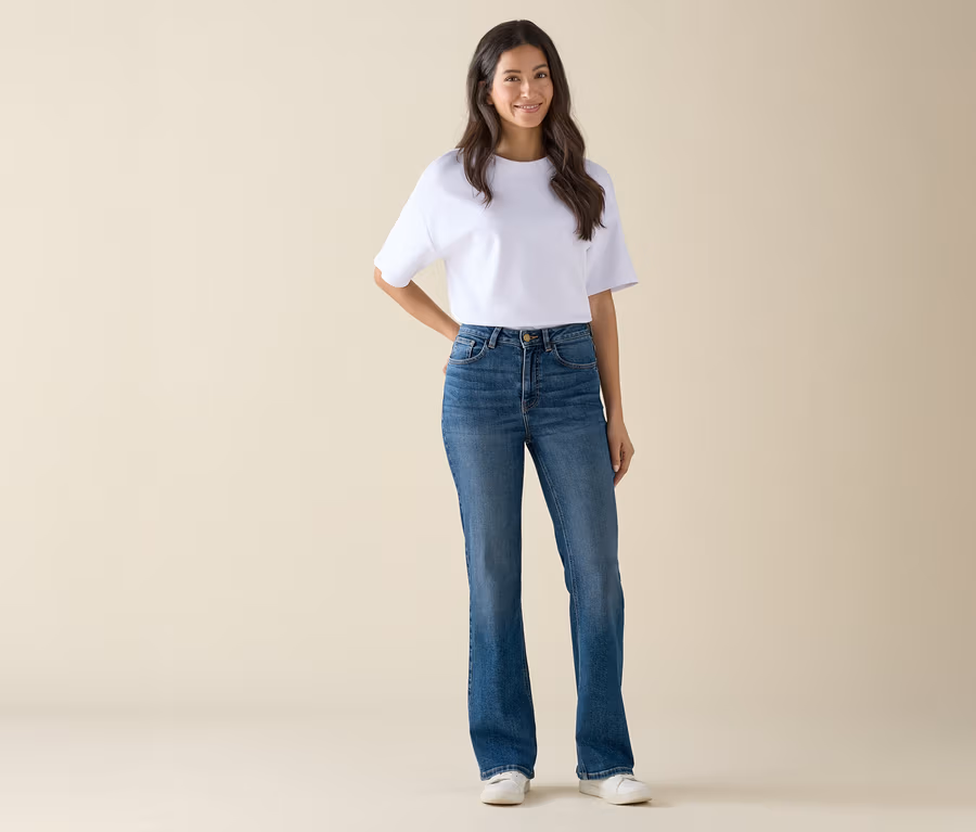 Frau in weißem T-Shirt und blauen Jeans steht und posiert.