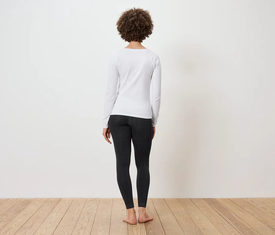Frau mit Afro-Frisur steht mit dem Rücken zur Kamera und trägt ein weißes Langarmshirt und schwarze Leggings.
