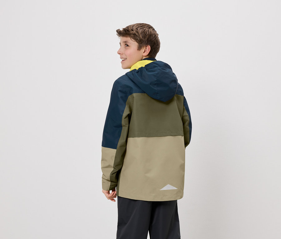 Ein Teenager steht mit dem Rücken zur Kamera und trägt eine farblich abgesetzte Jacke mit Kapuze in Blau, Oliv und Beige.