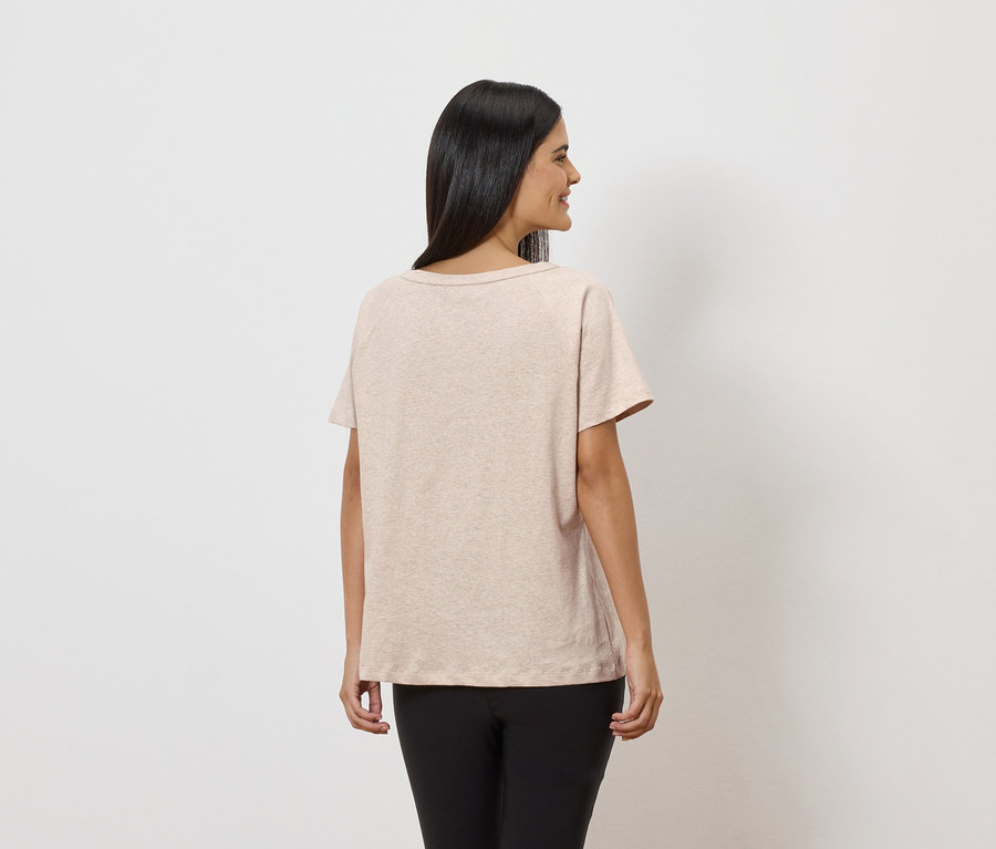Frau von hinten in beigem T-Shirt und schwarzen Leggings vor weißem Hintergrund.