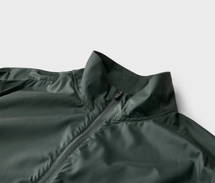 Nahaufnahme einer dunkelgrünen Jacke mit Reißverschluss und Stehkragen vor einem hellen Hintergrund.