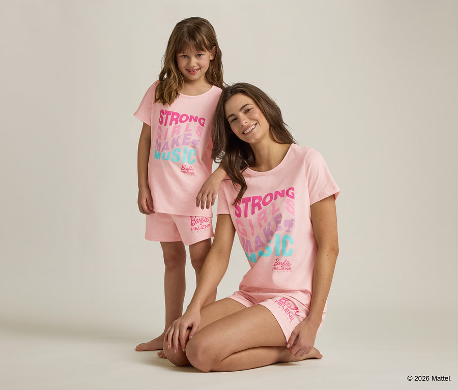 Eine junge Frau kniet neben einem Mädchen, beide tragen passende rosa Barbie-Schlafanzüge mit der Aufschrift "Strong Girls Make Music".