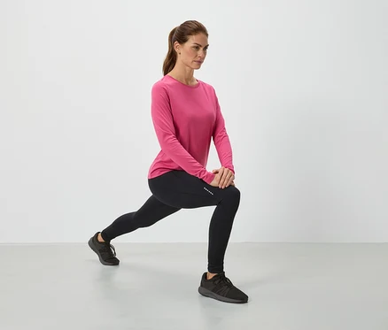 Frau in pinkem Oberteil und schwarzen Leggings dehnt sich.