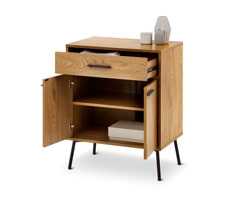 Heller Holzschrank mit schwarzen Beinen, einer geöffneten Schublade mit weißem Stoff und zwei offenen Türen, die ein Regal mit einer hellen Box zeigen. Zwei graue Vasen und ein weißer Behälter stehen oben.
