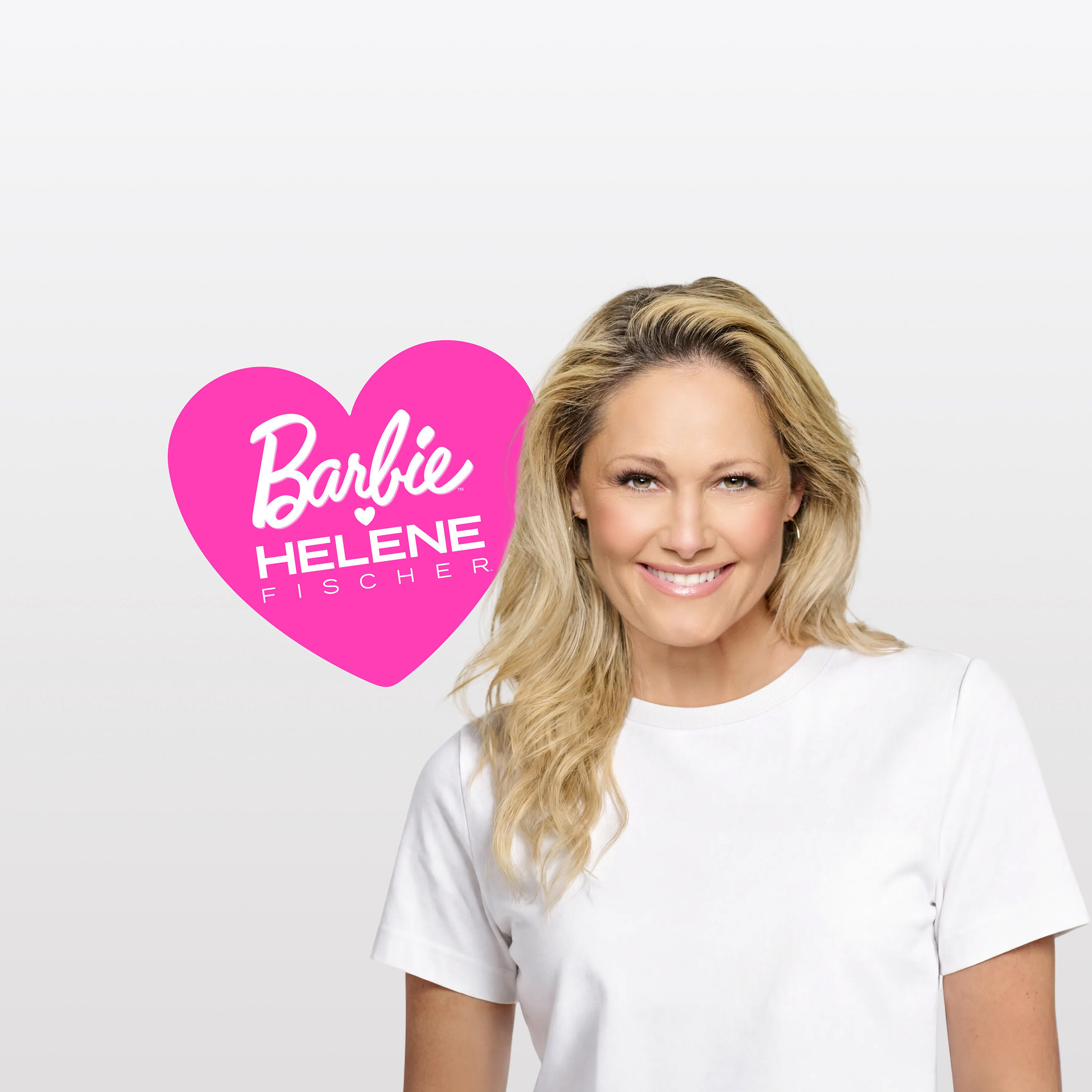 Helene Fischer, eine blonde Frau, lächelt in einem weißen T-Shirt, mit einer pinken Herzgrafik mit der Aufschrift „Barbie HELENE FISCHER“ links von ihr.