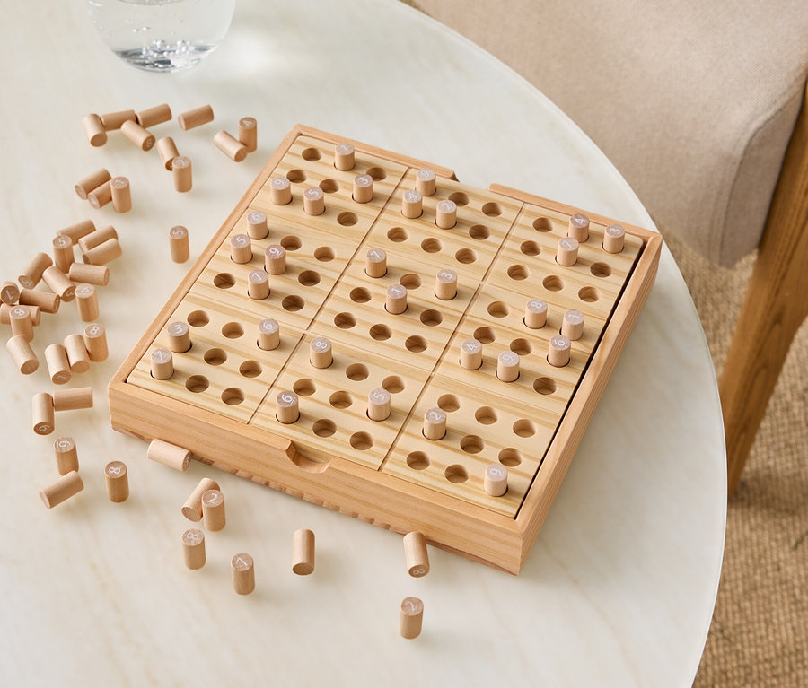 Holzspiel mit Stiften auf einem Tisch neben einem Glas Wasser.