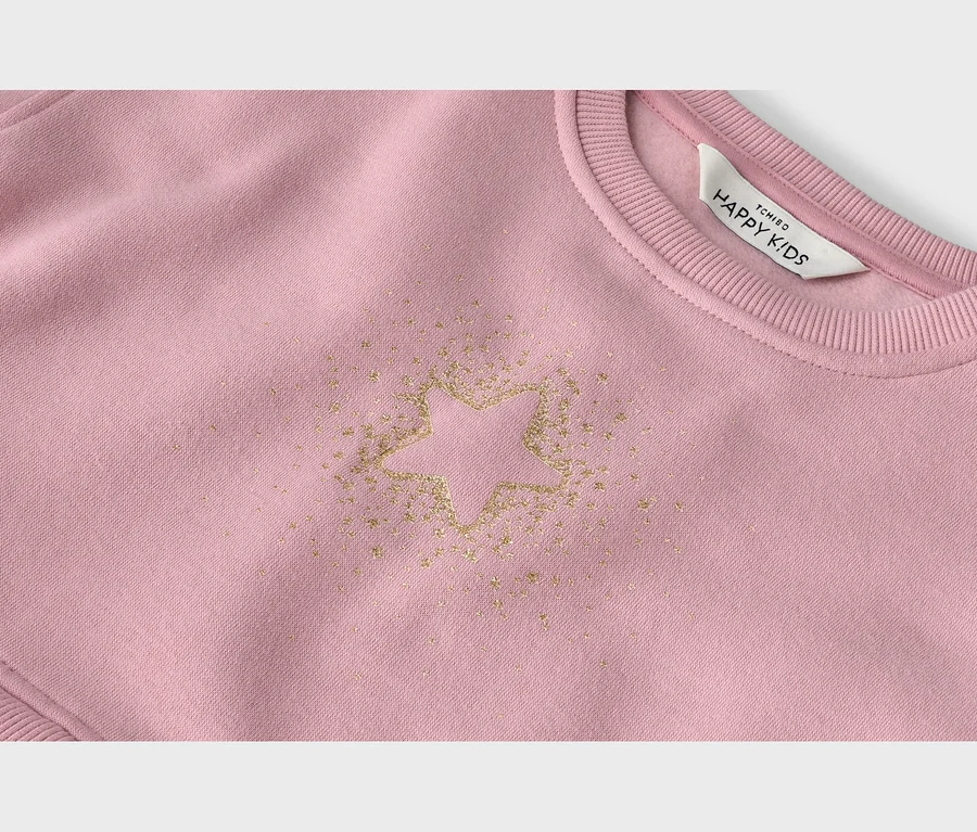 Rosa Sweatshirt mit goldenem Glitzerstern-Design auf der Vorderseite, umgeben von kleineren Glitzerpartikeln. Ein weißes Etikett mit „TCHIBO HAPPY KIDS“ ist am gerippten Kragen sichtbar.