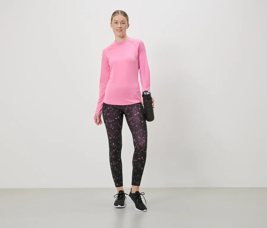 Frau in pinkem Langarmshirt und Leggings mit Blumenmuster hält eine schwarze Wasserflasche.