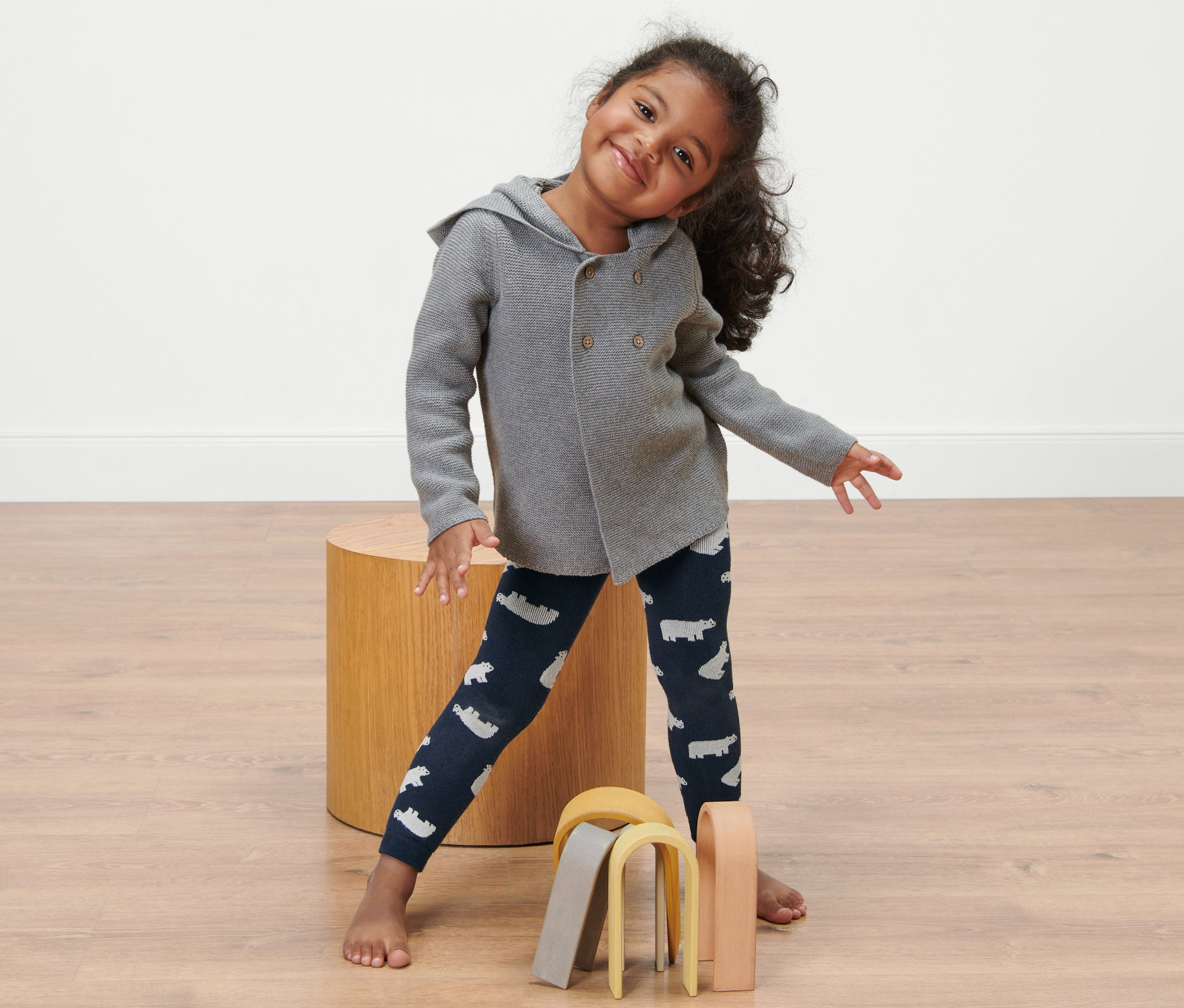 Ein lächelndes kleines Mädchen steht und trägt 2 Kleinkind-Thermoleggings mit Eisbärendruck und eine graue Strickjacke.