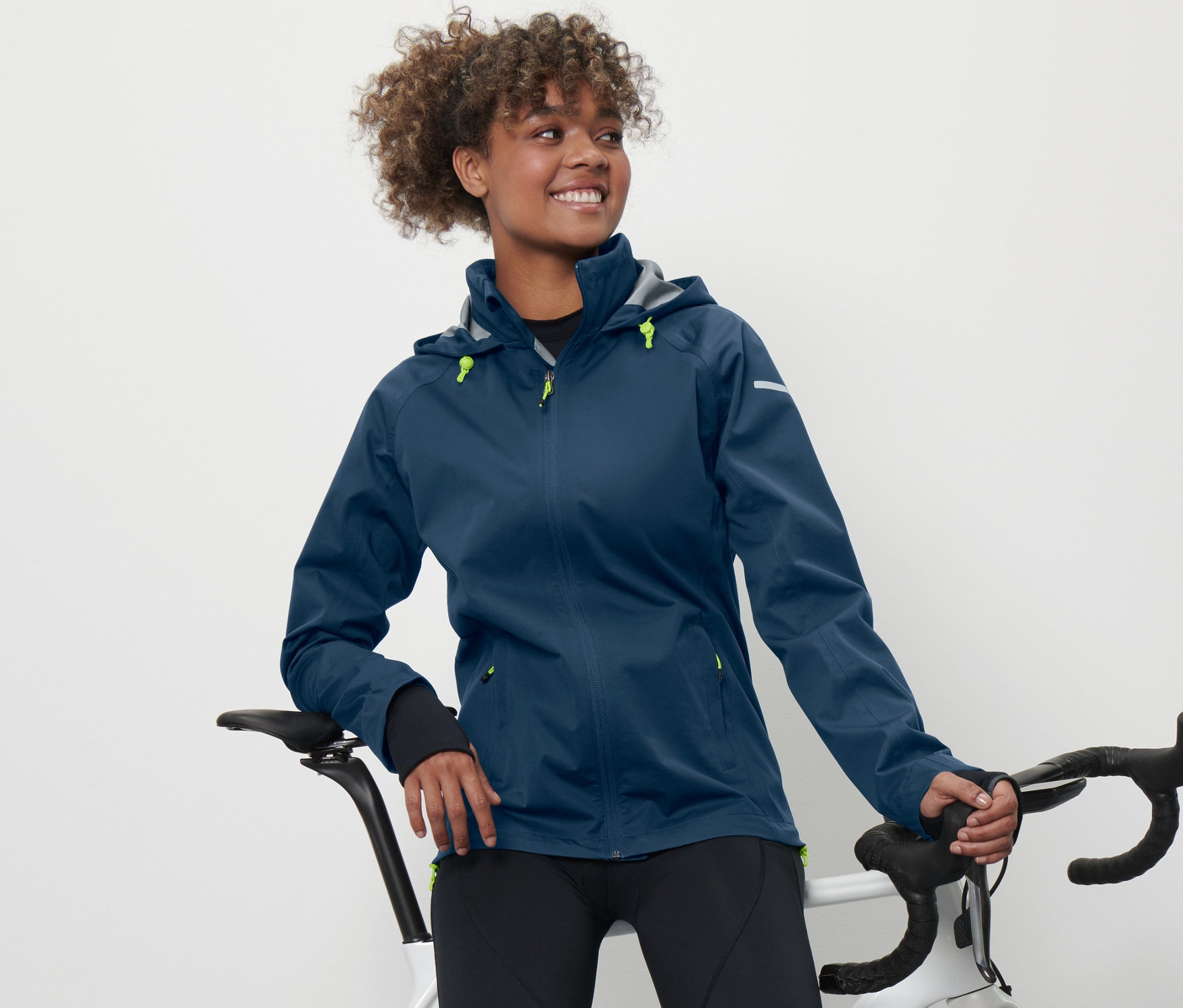 Eine Frau, die sich an ein Fahrrad lehnt, trägt eine Rad-Regenjacke.