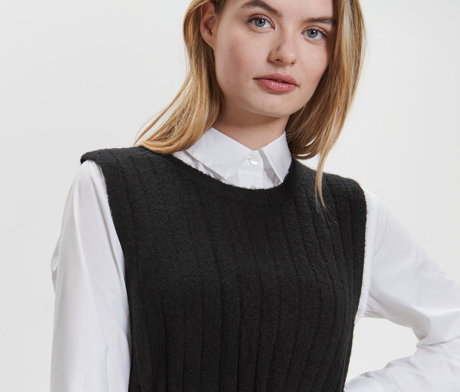 Blonde Frau trägt ein geripptes, schwarzes Strickkleid über einem weißen Hemd.