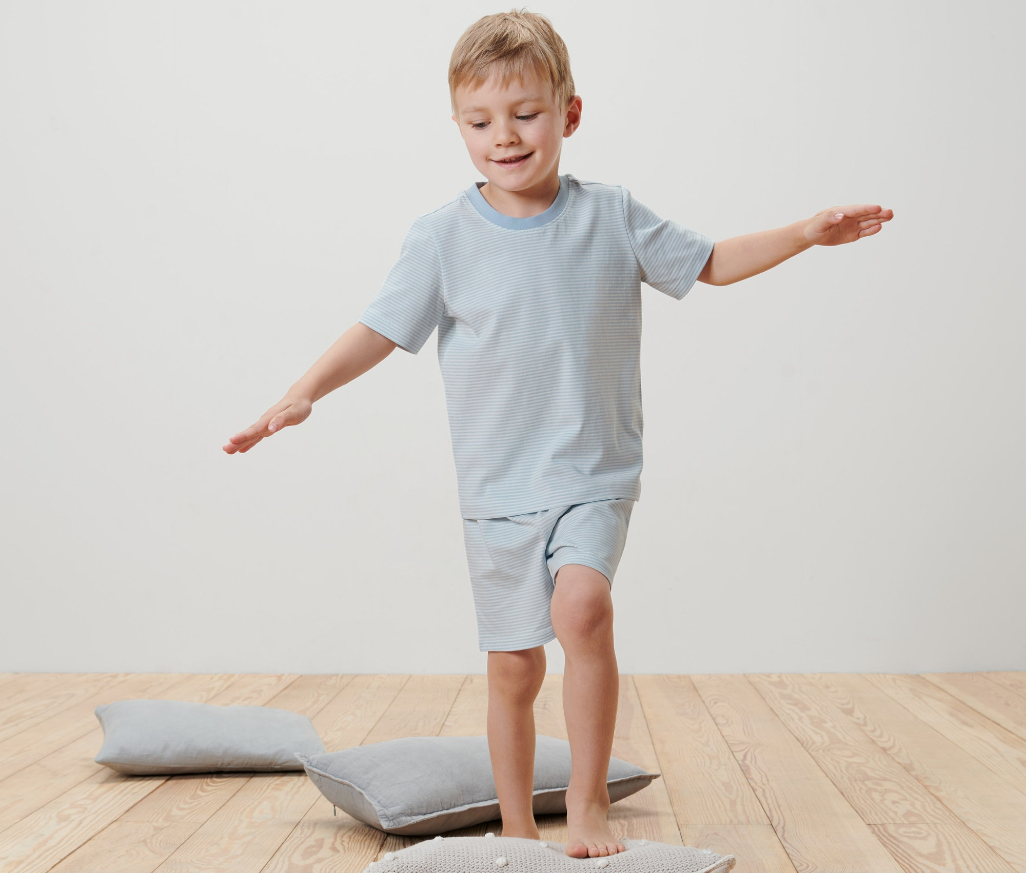 Ein Junge balanciert in einem Kinder-Shorty-Pyjama auf einem Kissen.
