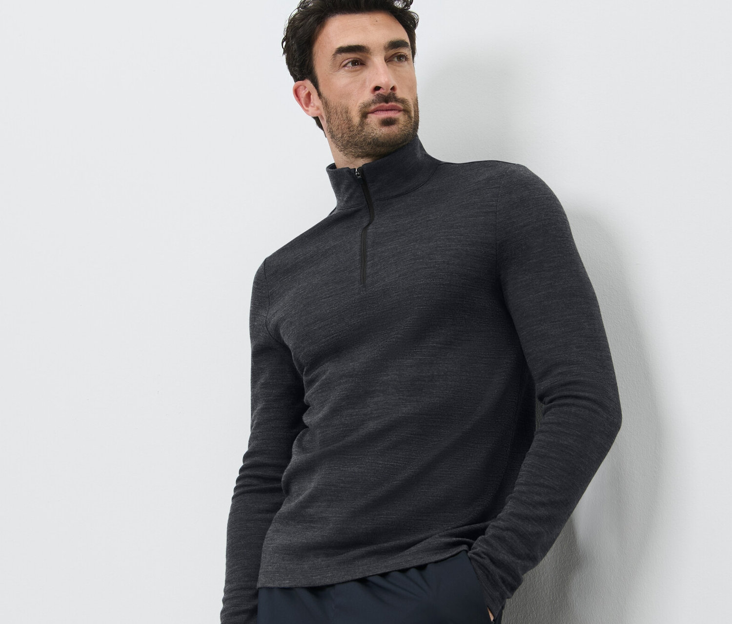 Mann posiert vor weissem Hintergrund und trägt ein Funktionsshirt mit RWS-zertifizierter Wolle und dunkle Hosen.