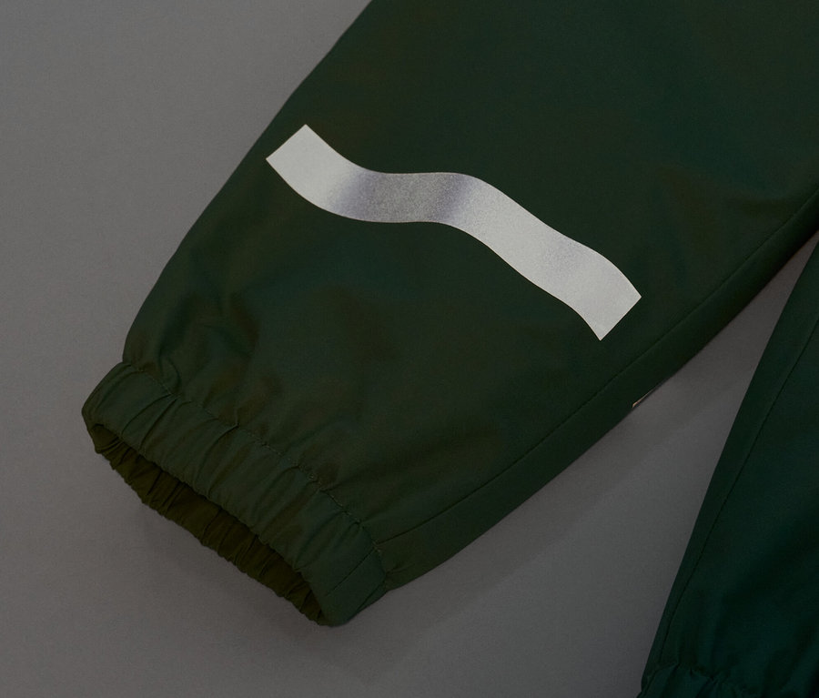 Detailaufnahme einer grasgrünen Kinder-Regenhose mit reflektierendem Streifen.
