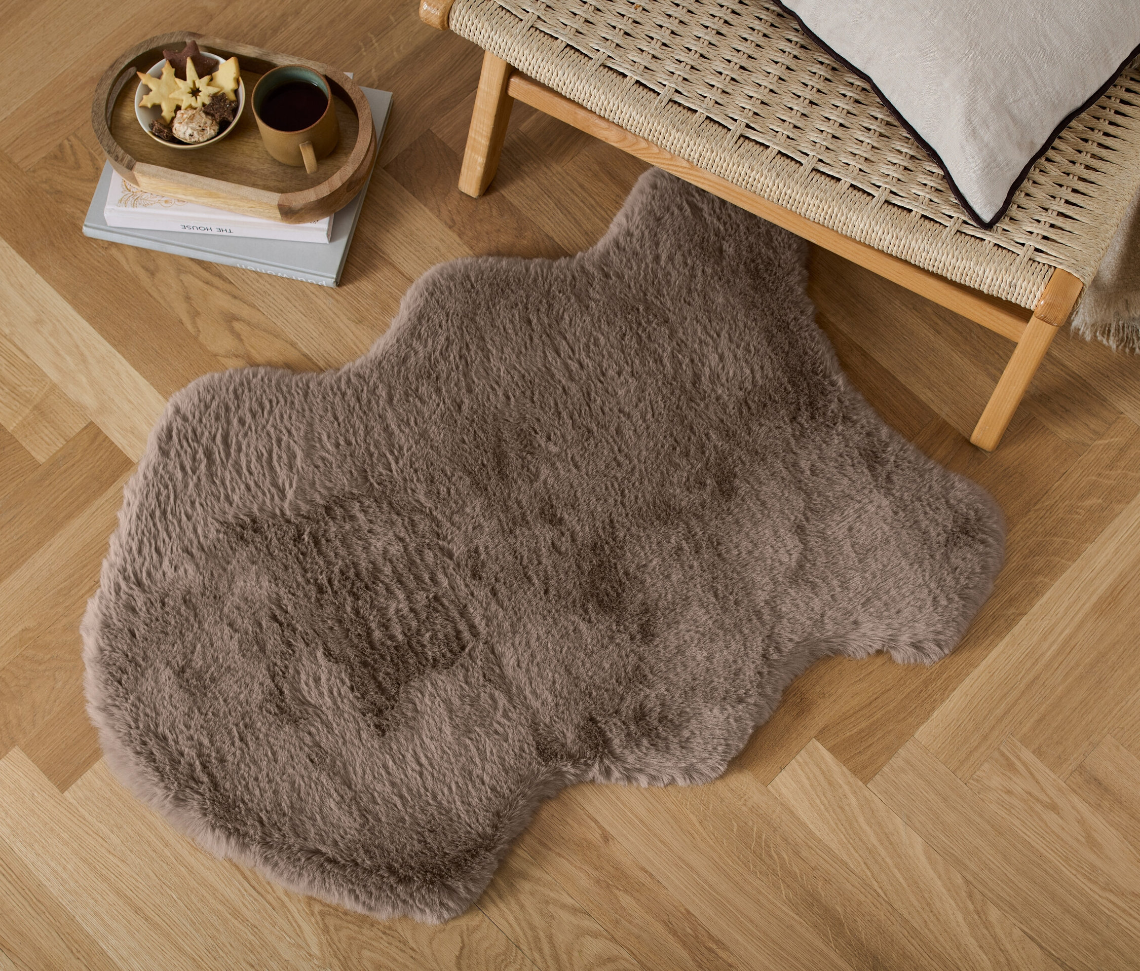 Ein Deko-Kunstfell liegt auf einem Holzboden neben einer Korbsitzbank.