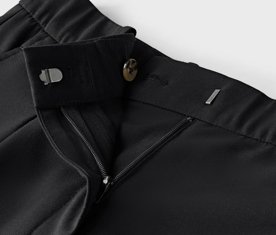 Detailaufnahme einer schwarzen Stoffhose mit Reißverschluss und Knopf.