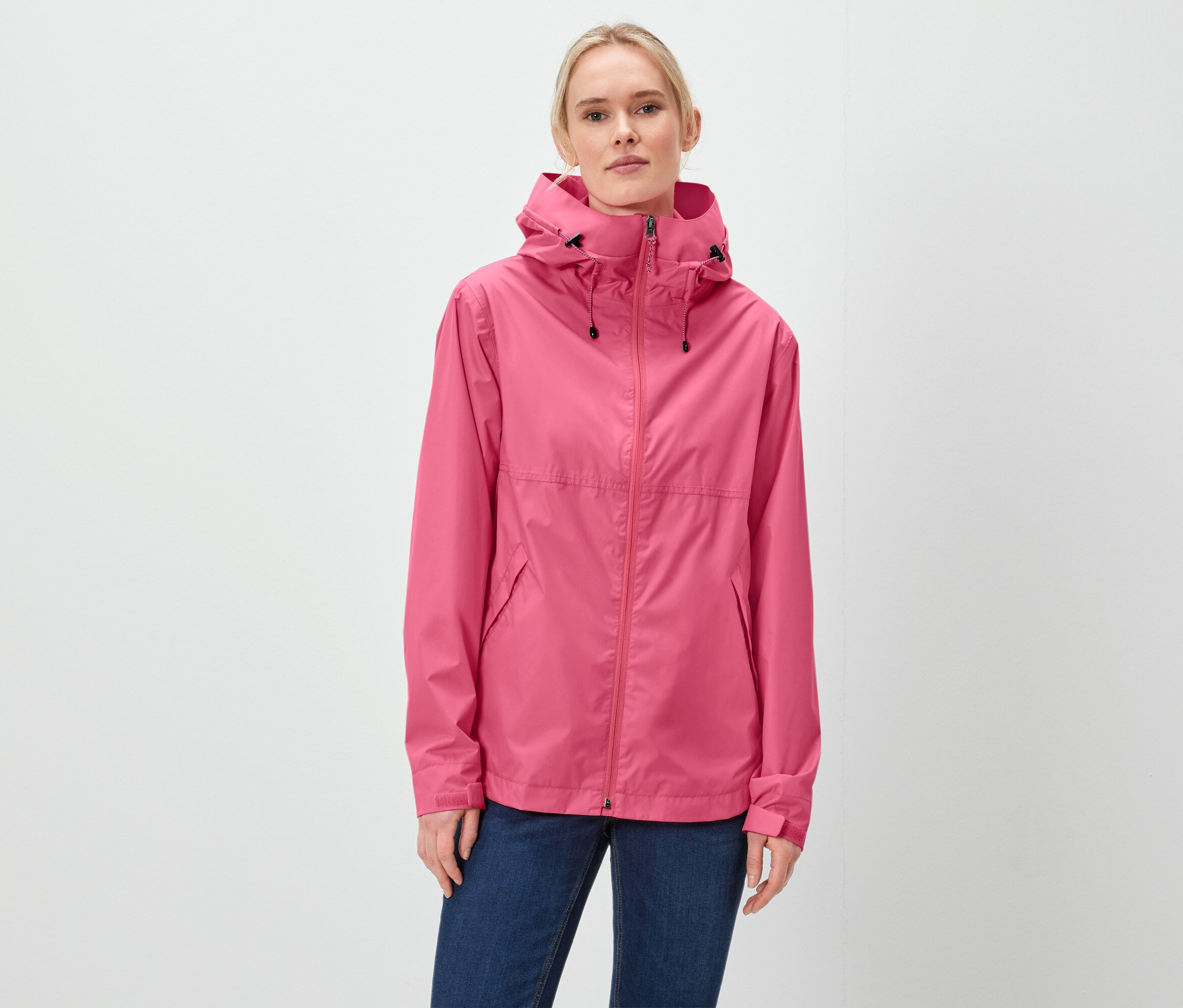 Eine Frau trägt eine pinke Jacke mit Kapuze und blaue Jeans.