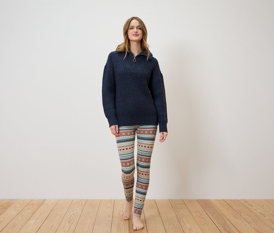 Eine Frau steht und trägt einen dunkelblauen Pullover und gemusterte Leggings.