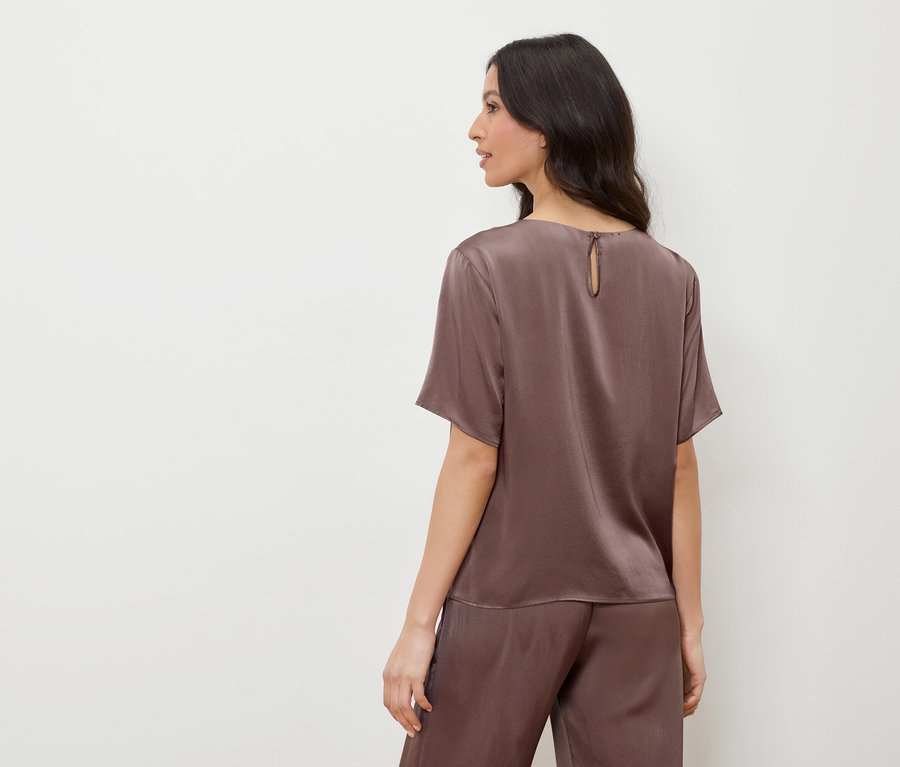 Frau in braunem Satin-Top und Hose, die nach links schaut.