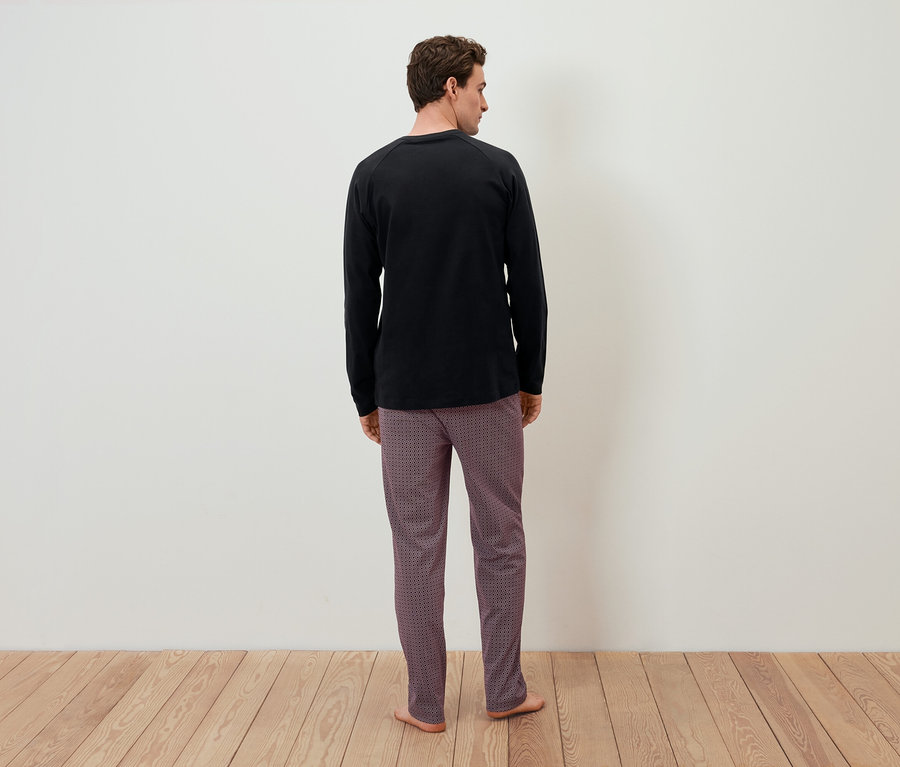Ein Mann mit dem Rücken zur Kamera trägt ein schwarzes Langarmshirt und gemusterte Hosen.