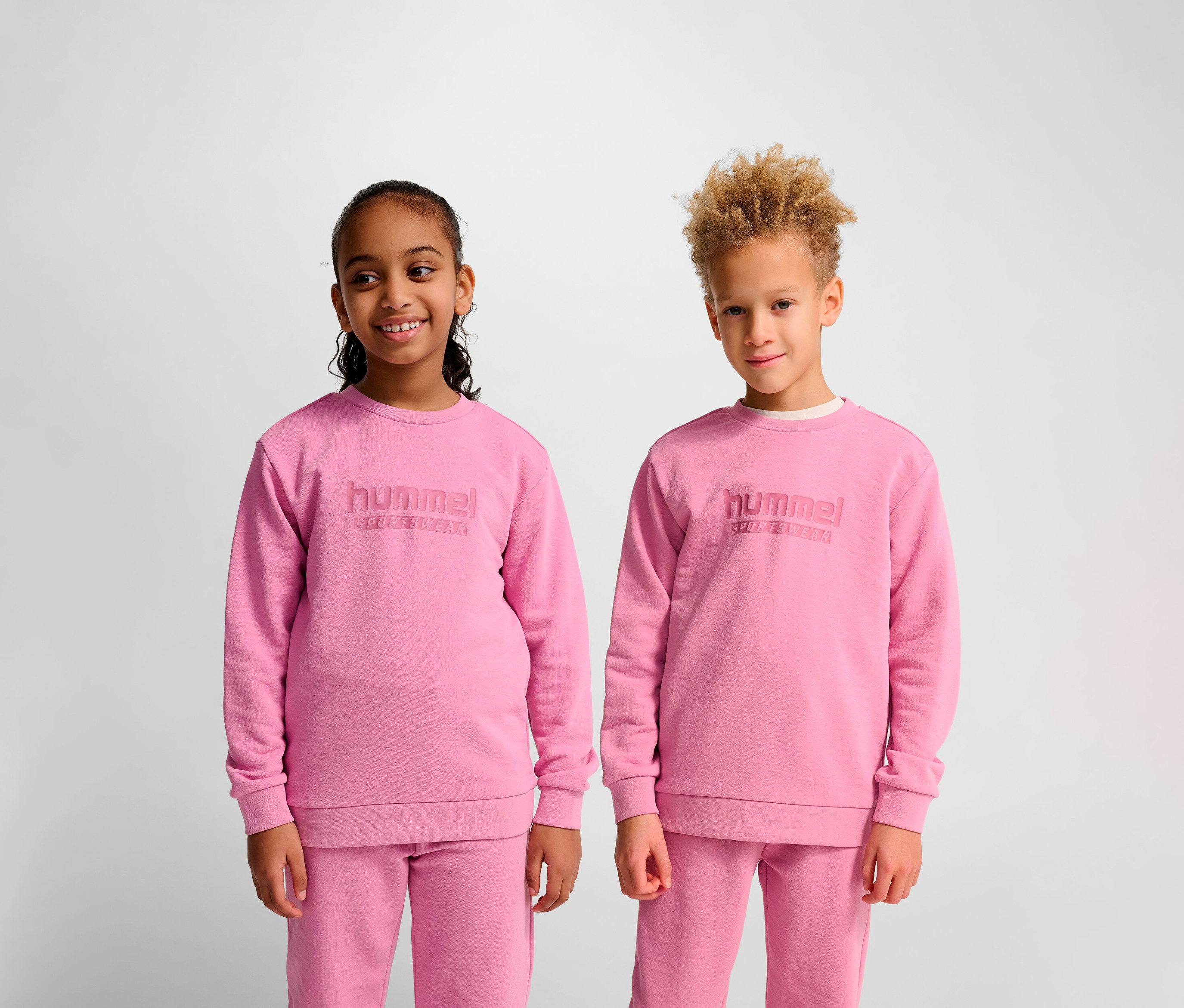 Zwei Kinder stehen nebeneinander und tragen rosa Hummel HMLJR Base-Sweatshirts.