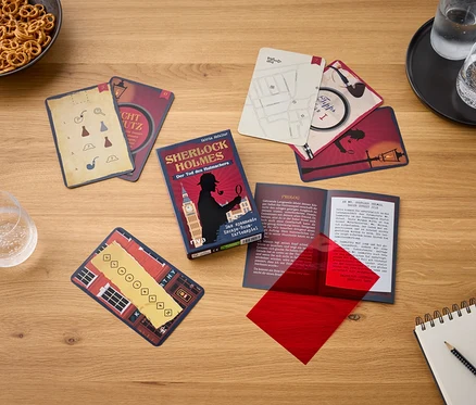 Auf einem Holztisch liegen das Spiel Sherlock Holmes: Der Tod des Hutmachers, Karten, ein Glas Wasser, Brezeln und ein Notizblock.