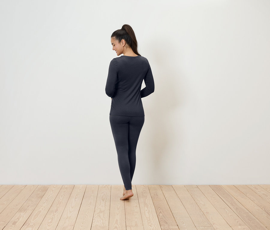 Frau steht mit dem Rücken zur Kamera und trägt dunkelgraue Thermounterwäsche.