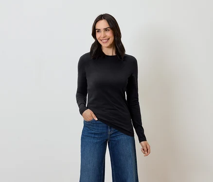 Frau mit braunen Haaren posiert in einem schwarzen Langarmshirt und blauen Jeans.