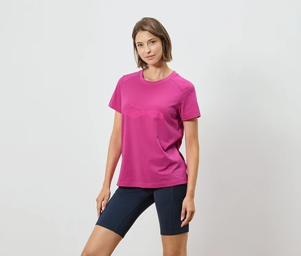 Frau trägt ein pinkes T-Shirt mit einer Bergkette und dunkelblaue Shorts vor einem weißen Hintergrund.