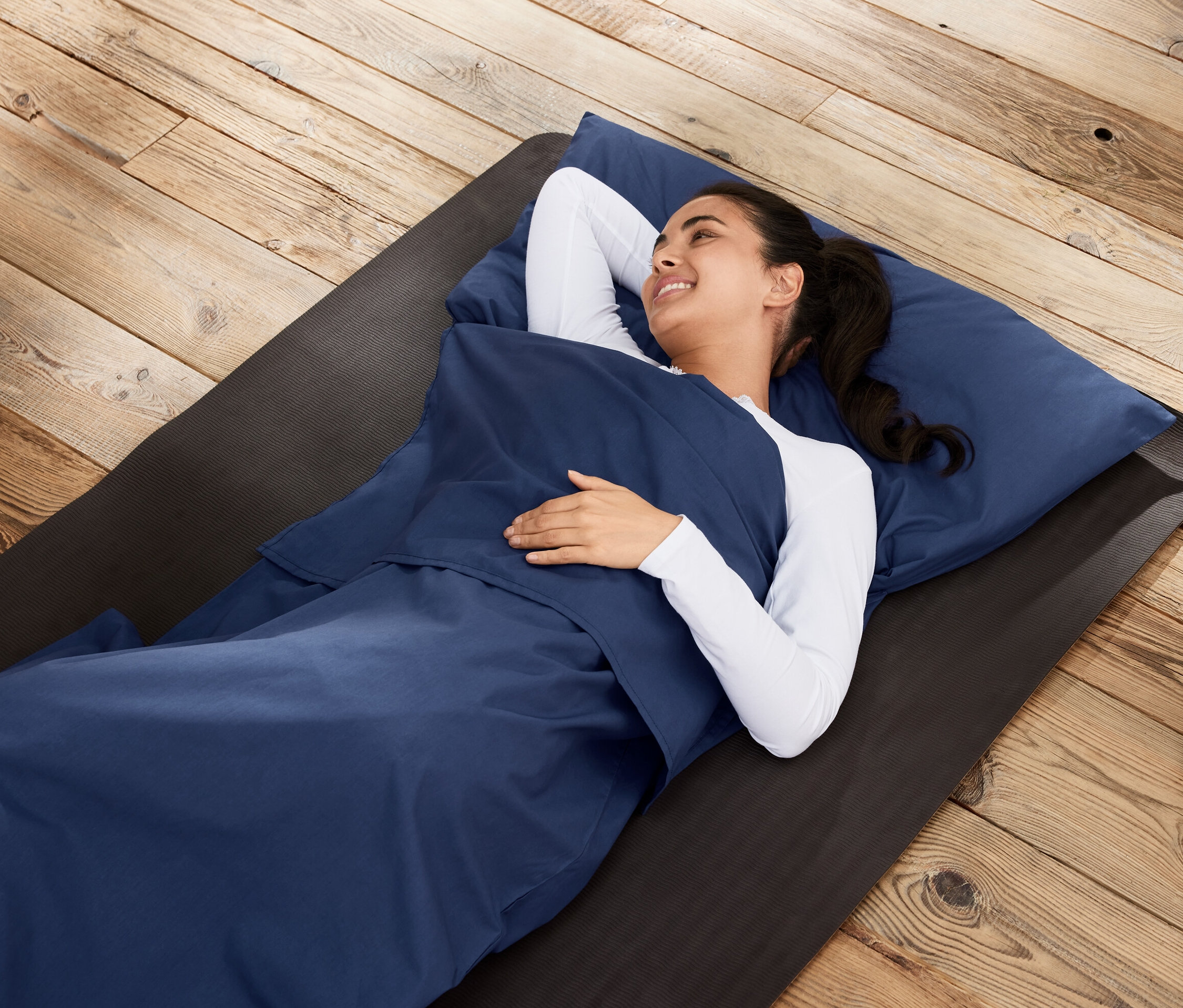 Frau liegt in Schlafsack-Inlay auf einer Matte auf Holzboden.