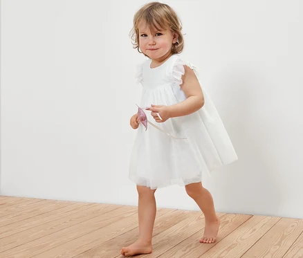 Kleines Mädchen in einem Baby-Tüllkleid geht über einen Holzboden.