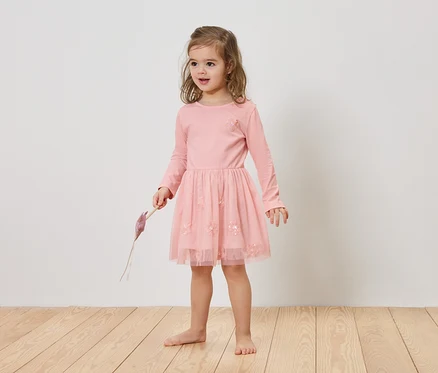 Mädchen mit blonden Haaren trägt ein rosa Kleid und hält einen lila Gegenstand in der Hand.