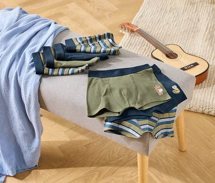 Auf einer Bank liegen eine blaue Decke und mehrere Boxershorts in Grün, Dunkelblau und mit Streifenmuster. Eine kleine Gitarre steht daneben.