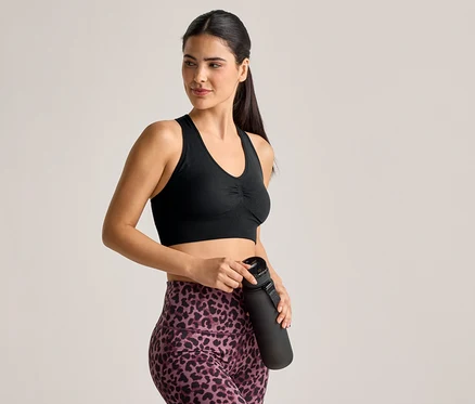 Frau im Sport-BH und Leggings mit Leopardenmuster hält eine schwarze Wasserflasche.