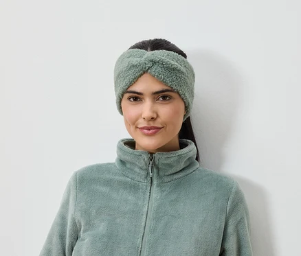 Frau mit olivgrünem Stirnband und Fleecejacke vor weißem Hintergrund.