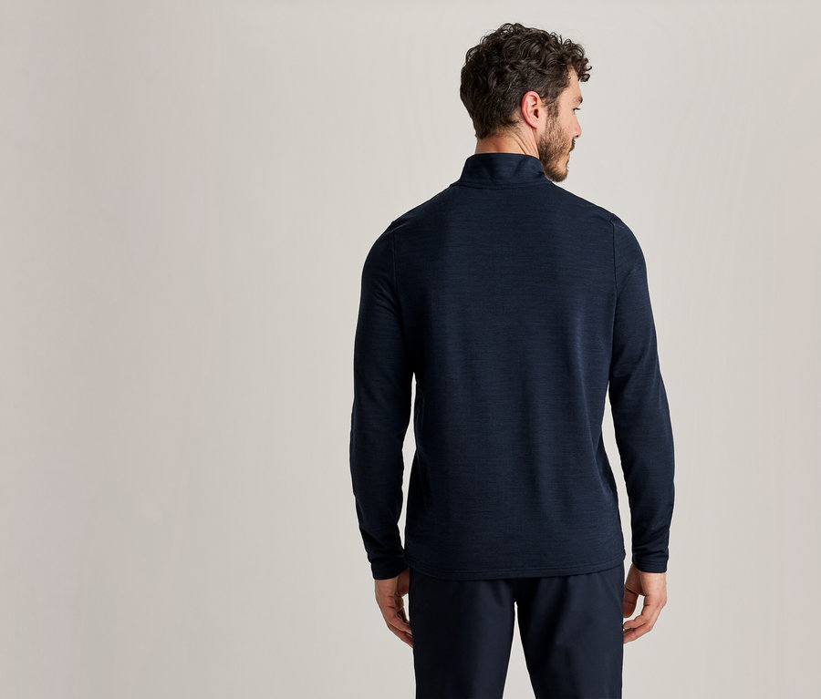 Mann von hinten in einem dunkelblauen Langarmshirt und dunkelblauer Hose vor hellem Hintergrund.