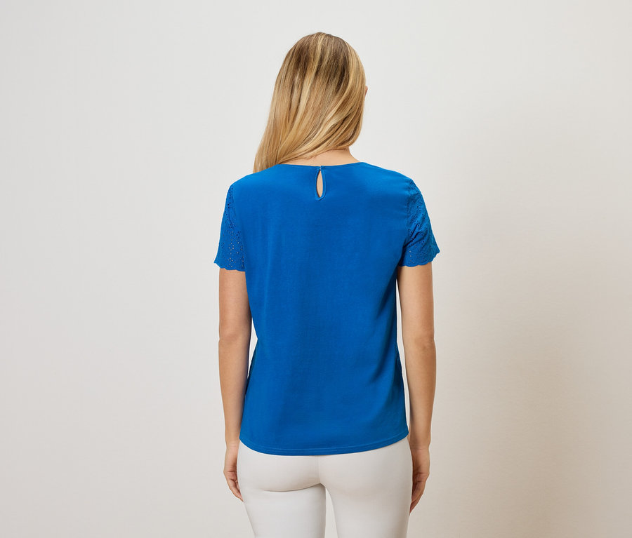 Rückansicht einer Frau mit langen blonden Haaren, die ein blaues T-Shirt und weiße Hosen trägt.