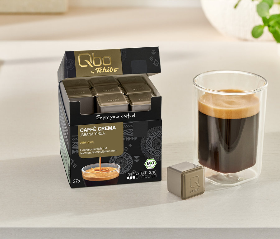 Geöffneter Karton Qbo Caffè JABANA YIRGA mit Kapseln, Tasse Kaffee und einzelne Kapsel auf einer hellen Oberfläche.